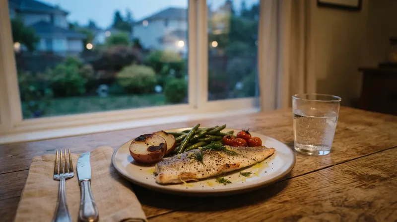 A dinner plate with grilled trout, green beans, a roasted potato and cherry tomatoes beside a glass of water